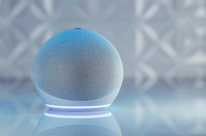 A sleek smart speaker with neon glow on reflective surface, showcasing modern technology.