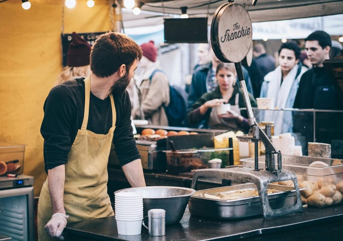 Dynamic scene of a street food vendor working in a busy market, engaging with diverse customers.